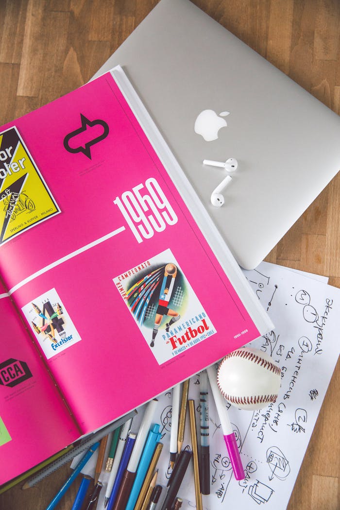 A creative workspace featuring a colorful open book, laptop, and drawing materials, ideal for design inspiration.